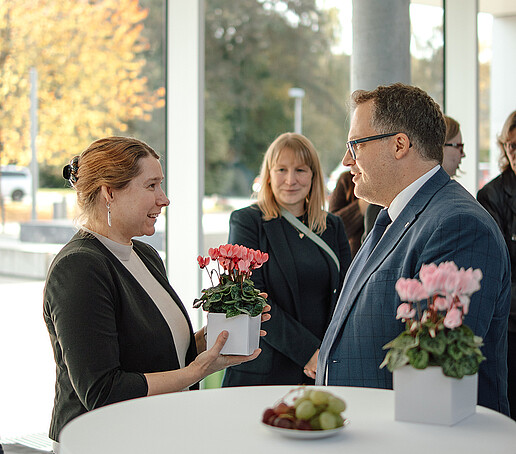 A professor holds a flower arrangement in her hands and talks to the rector.