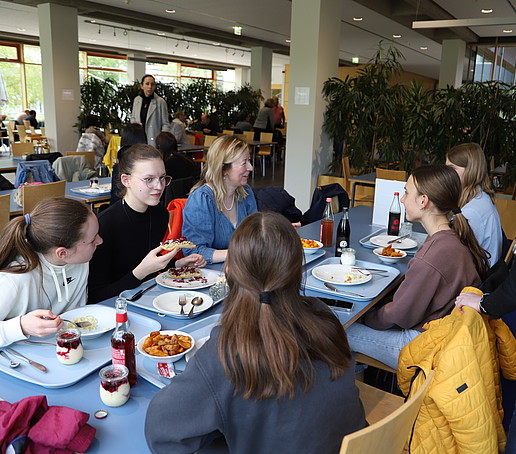 The principal is sitting at a table in the canteen talking to schoolgirls.