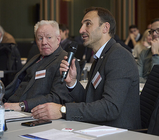 Prof. Schütte sitzt am Platz  neben Prof. Kästner und spricht in ein Mikrofon.