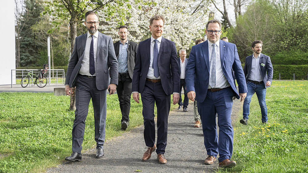 Die Teilnehmenden der Baumpflanzung gehen auf einem von Bäumen gesäumten Weg auf dem Zittauer Campus.