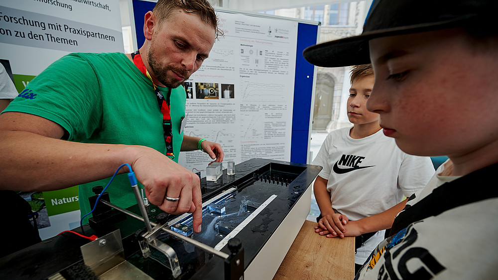 An HSZG employee explains fluid mechanics to students at the stand.