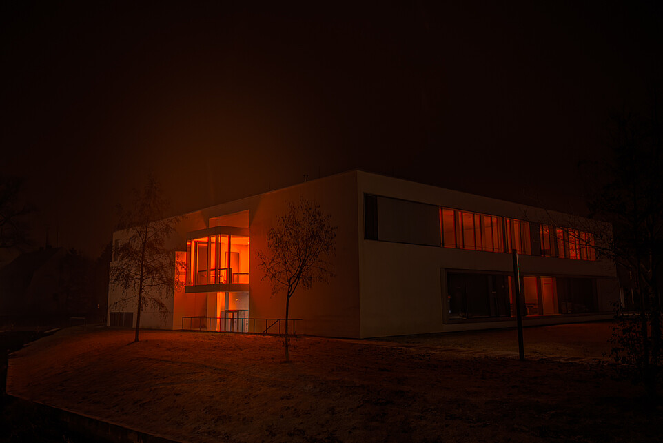 Nach Sonnenuntergang erstrahlt aus den Fenstern des Gebäudes Z vier orangenes Licht.