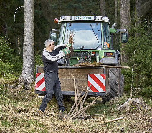 Ein Forstmitarbeiter vor einem Traktor im Wald.