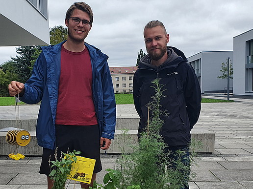 Zwei junge Männer stehen auf dem Zittauer Campus. Einer hält ein Bienenhotel in der Hand.