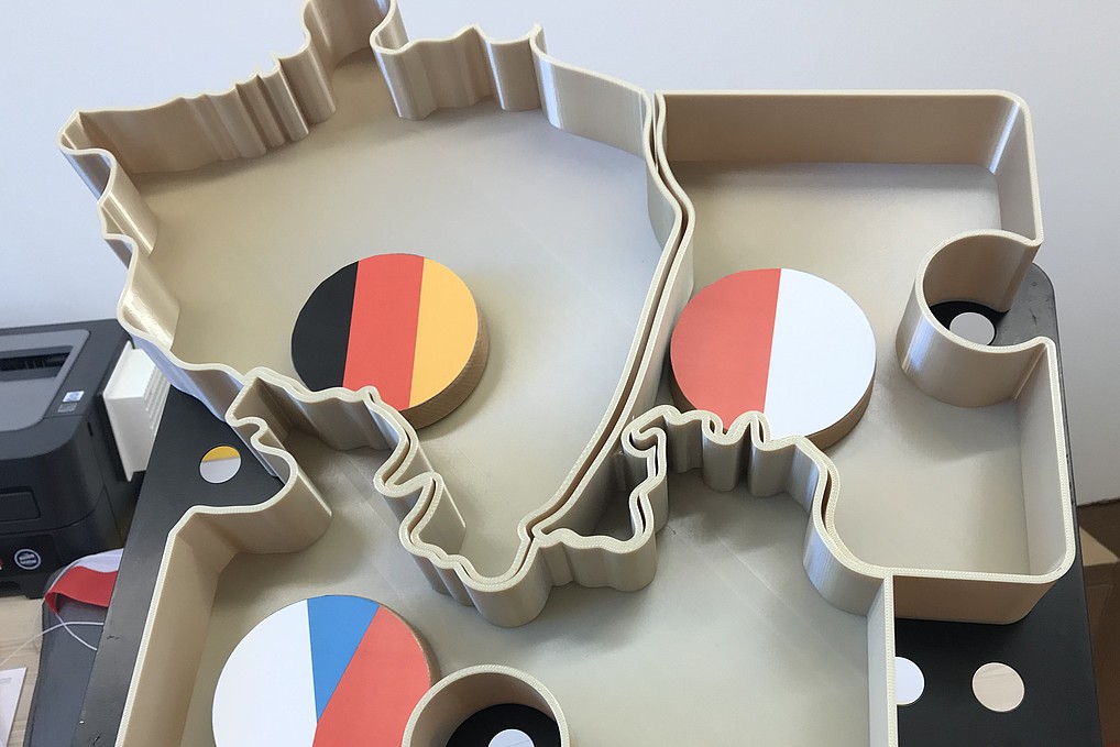 Dargestellt ist ein 3D-Druckmodell der Region Dreiländereck Deutschland, Polen und Tschechien. Die drei Länder werden durch runde Scheiben welche die jeweilige Flaggen symbolisieren dargestellt. 