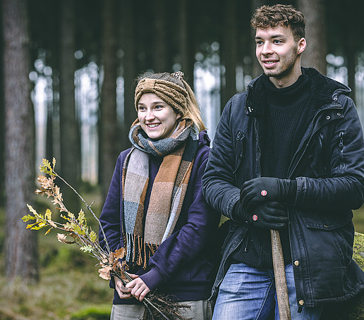 Zwei Studierende stehen lächeln im Wald.