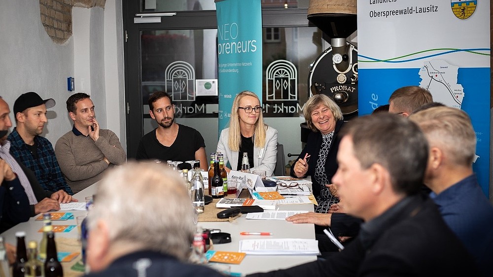 Teilnehmende an den Vorbereitungen des Erzählsalons sitzen am Tisch und untrhalten sich.