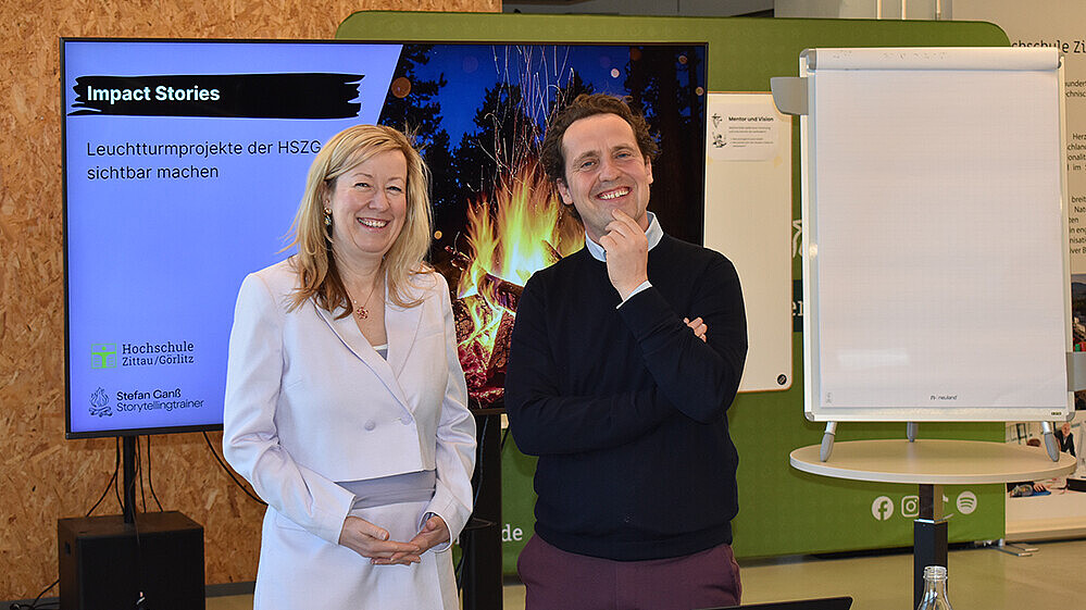 Vice President Prof. Dr. Sophia Keil and TV and media expert Stefan Ganß stand next to each other in front of a screen and smile into the camera.