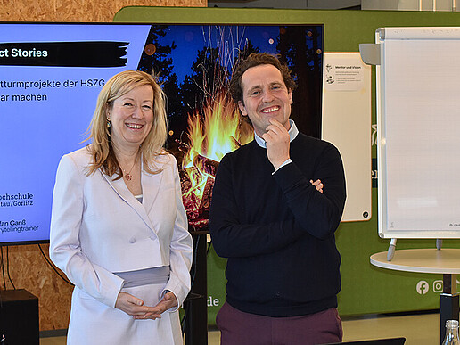 Vice President Prof. Dr. Sophia Keil and TV and media expert Stefan Ganß stand next to each other in front of a screen and smile into the camera.