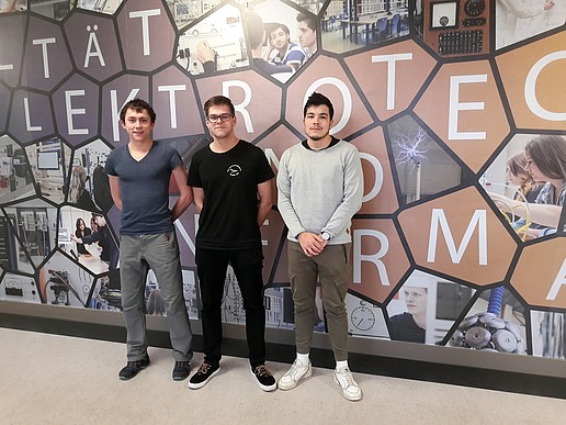 3 young KIA students in front of wall with graphics in house 1 first floor