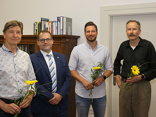 Der Rektor und drei HSZG-Mitarbeiter stehen im Büro des Rektors und lächeln in die Kamera. Die Mitarbeiter haben eine Blume in der Hand als Dank für die Abordnung in die Gesundheitsämter der LK Bautzen und Görlitz..