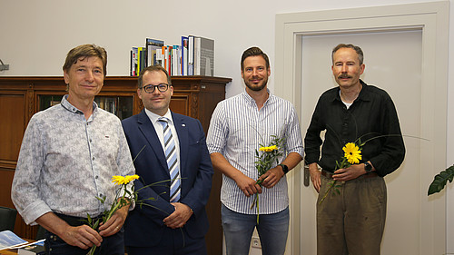 Der Rektor und drei HSZG-Mitarbeiter stehen im Büro des Rektors und lächeln in die Kamera. Die Mitarbeiter haben eine Blume in der Hand als Dank für die Abordnung in die Gesundheitsämter der LK Bautzen und Görlitz..