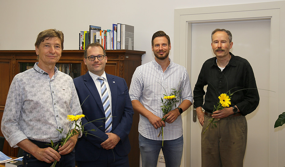 Foto: Jens Freudenberg Der Rektor und drei HSZG-Mitarbeiter stehen im Büro des Rektors und lächeln in die Kamera. Die Mitarbeiter haben eine Blume in der Hand als Dank für die Abordnung in die Gesundheitsämter der LK Bautzen und Görlitz..