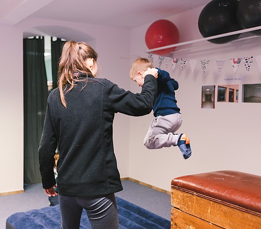 kleiner Junge springt vom Turngerät an der Hand er erwachsenen Person