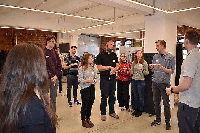Workshop participants stand next to each other in the Celsiuz workroom and discuss a task.
