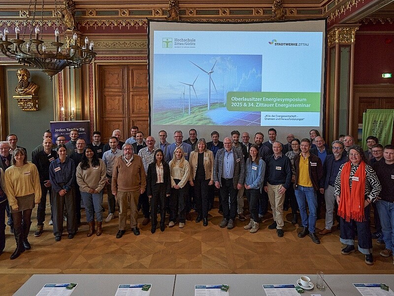 A group of people stand next to each other in the town hall of Zittau and smile into the camera.