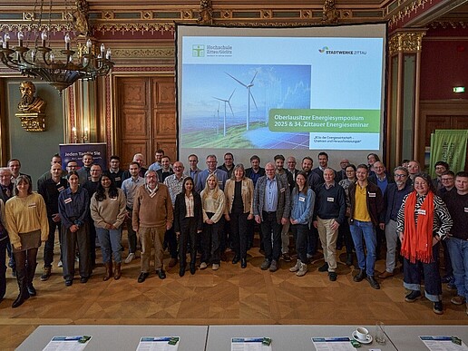 Im Bürgersaal des Zittauer Rathauses steht eine Gruppe Menschen nebeneinander und lächeln in die Kamera.