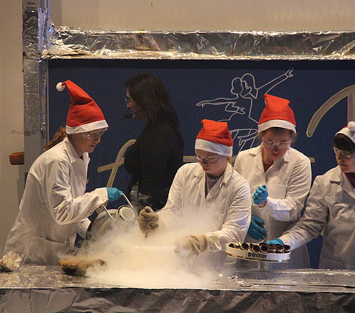 Four chemists in Christmas hats conduct a steamy experiment on stage.