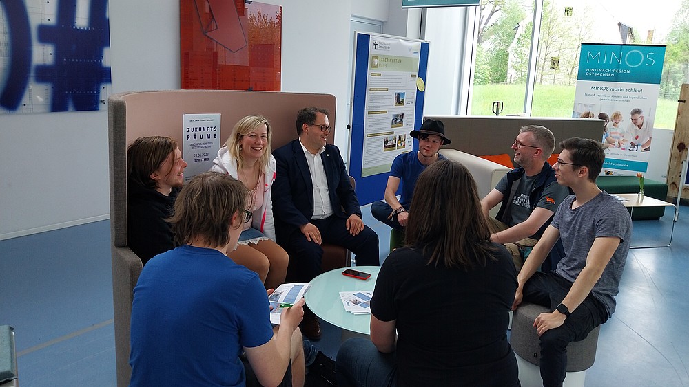 Rektor und Prorektorin sitzen mit Studierenden in der Möbelausstellung.