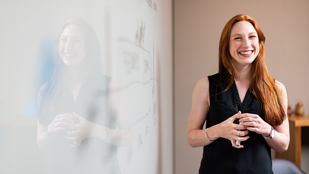 A young woman stands laughing next to a whiteboard.