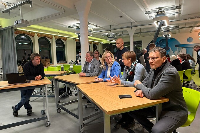 Professor Keil and counselors sit at tables in the School Lab and talk.