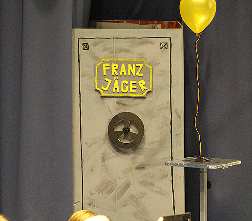 A gray safe with a yellow balloon stands on the stage.