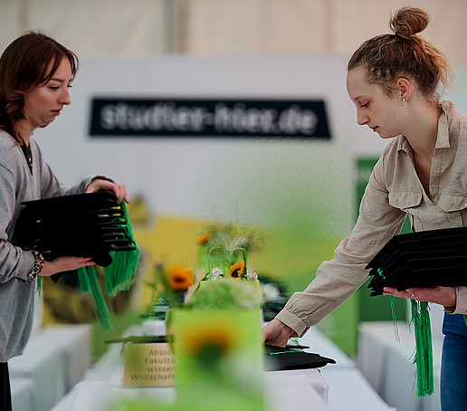 Studentische Hilfskräfte legen Absolventenhüte auf die Tische.