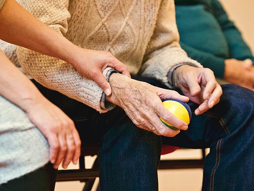 The hand of a younger person presses on the wrist of an older person holding a stress ball.