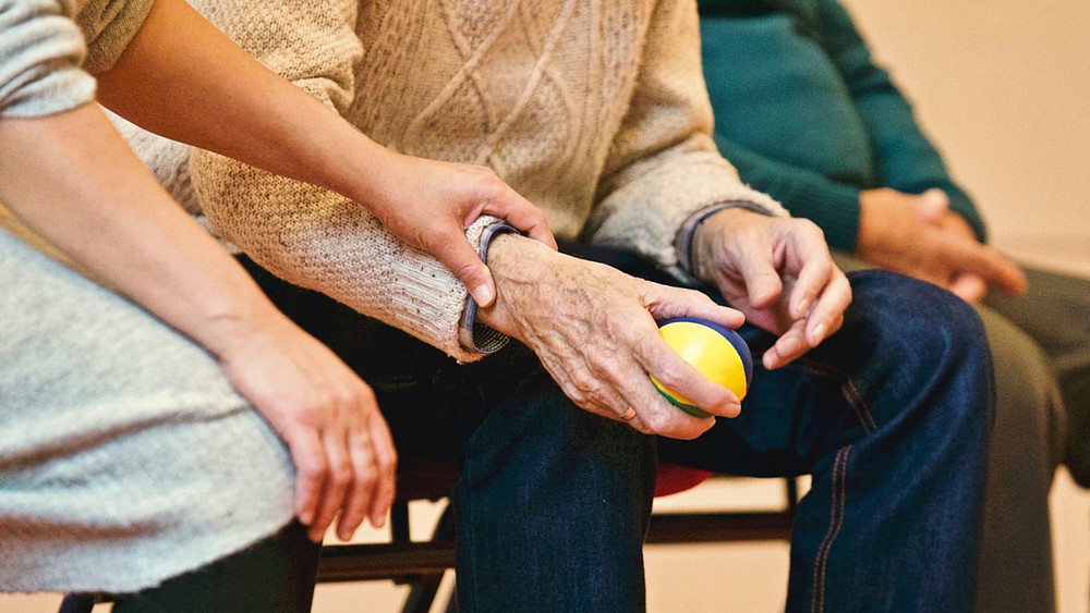 The hand of a younger person presses on the wrist of an older person holding a stress ball.