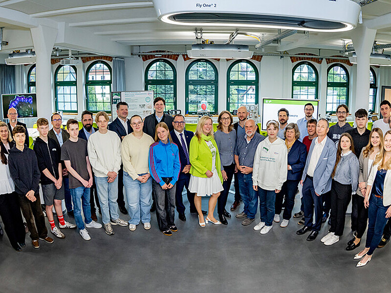 The guests at the event stand next to each other in the School Lab and smile into the camera.
