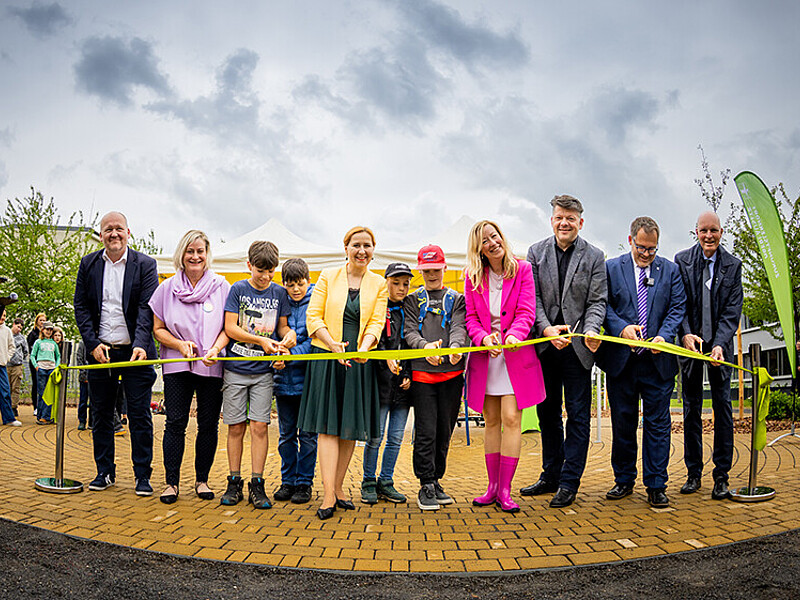 A group photo of the guests of honor as they cut the ribbon in front of the green classroom with golden scissors.