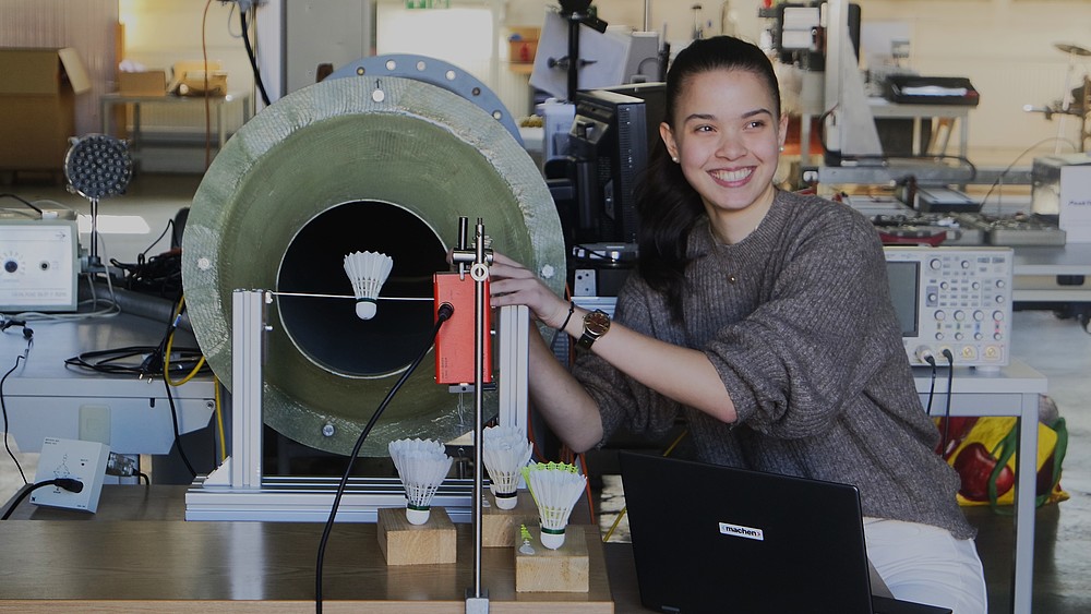 Helena is squatting next to a flow system with a shuttlecock stretched out in front of it.