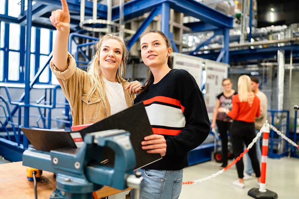 Zwei Studentinnen stehen im Zittauer Kraftwerkslabor. Die Blicke fallen in die Richtung auf die eine der Studentinnen deutet. 