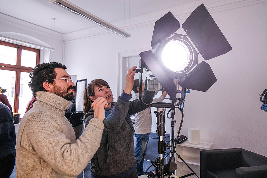 In einem Seminarraum arbeiten zwei Personen an einer Filmlampe.