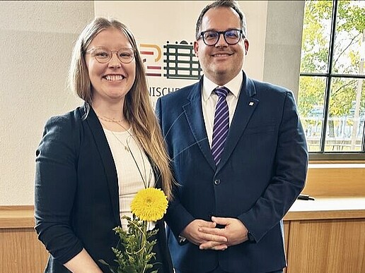 Professor Schellhammer stands next to Rector Kratzsch and holds a yellow flower in her hand, both smiling into the camera.
