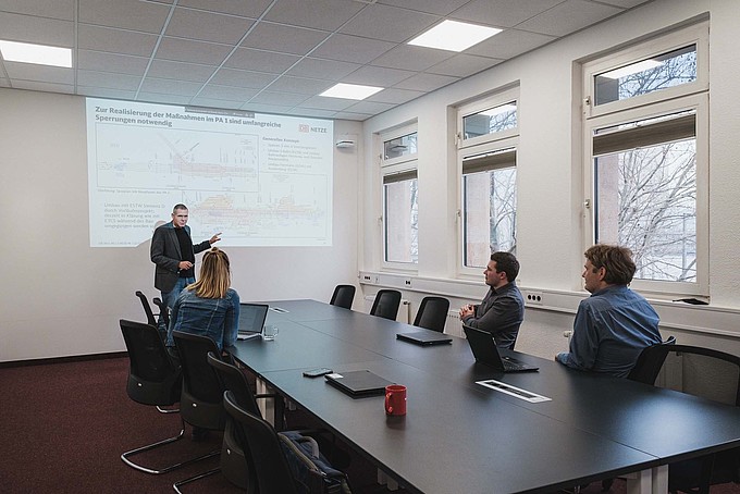 In a conference room, a man gives a presentation to an audience of three.