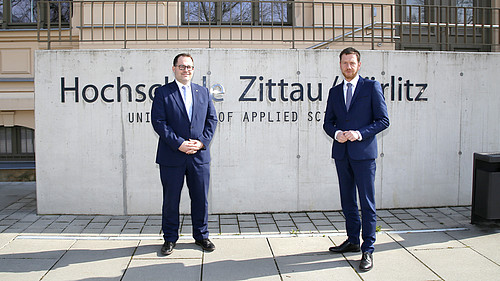 Der Rektor und Ministerpräsident stehen vor dem HSZG-Schriftzug vor Haus Z I.