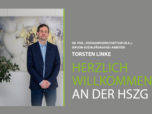 Prof. Linke steht vor einem Gemälde im Haus I der HSZG. Er trägt einen dunkelblauen Anzug und guckt stolz in die Kamera. Er wurde am 1.3.20 an die HSZG berufen. 