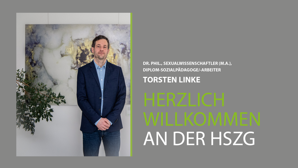 Prof. Linke steht vor einem Gemälde im Haus I der HSZG. Er trägt einen dunkelblauen Anzug und guckt stolz in die Kamera. Er wurde am 1.3.20 an die HSZG berufen. 