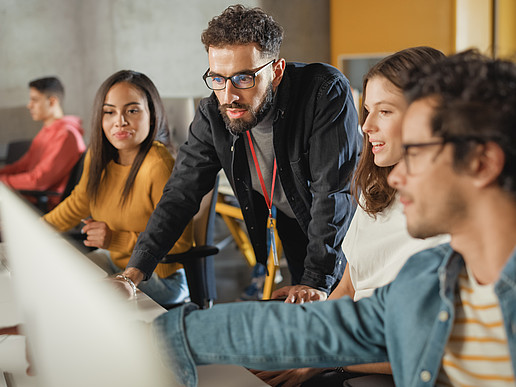 A group of students are chatting and pointing at a laptop.