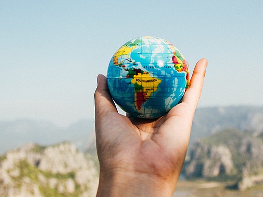 An outstretched hand holds an earth globe, in the background I can see rocky mountain formations.