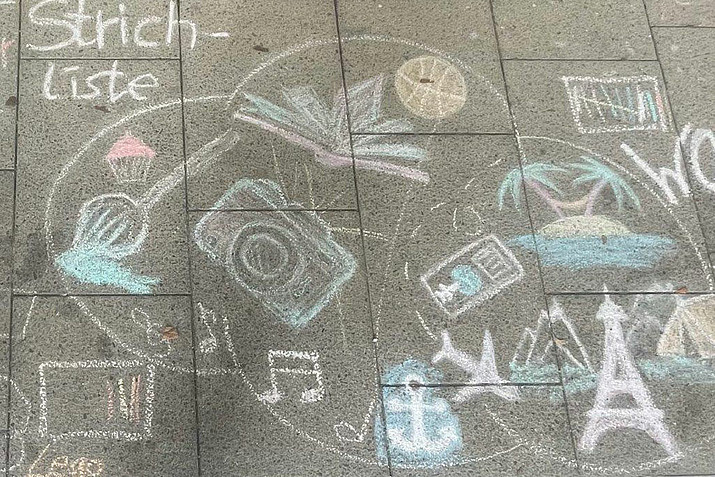 Chalk drawing on the asphalt with symbols such as a camera, Eiffel Tower, airplane, anchor, island, basketball, etc.