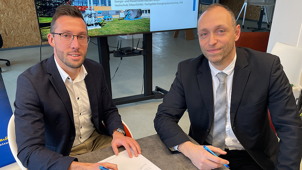 The head of the EWB division and Prof. Kunick from the HSZG sign the cooperation agreement at a table.