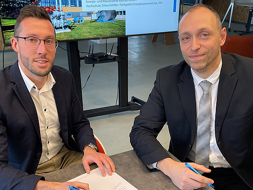The head of the EWB division and Prof. Kunick from the HSZG sign the cooperation agreement at a table.