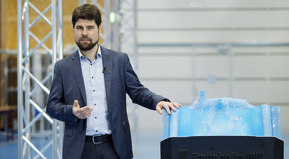 Professor Sebastian Scholz stands next to a lightweight component in a production hall.