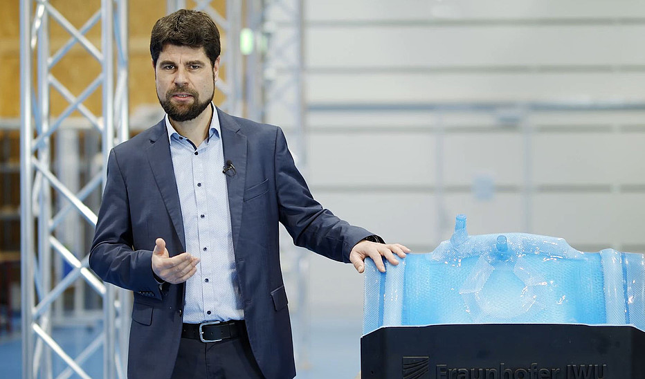 Foto: Fraunhofer IWU Professor Sebastian Scholz steht neben einem Leichtbauteil in einer Fertigungshalle.