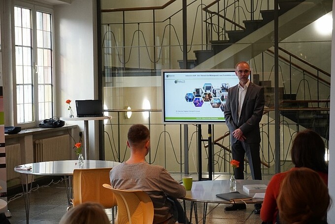 Prof. Wendt speaks next to a screen, addressing the audience seated at round tables.