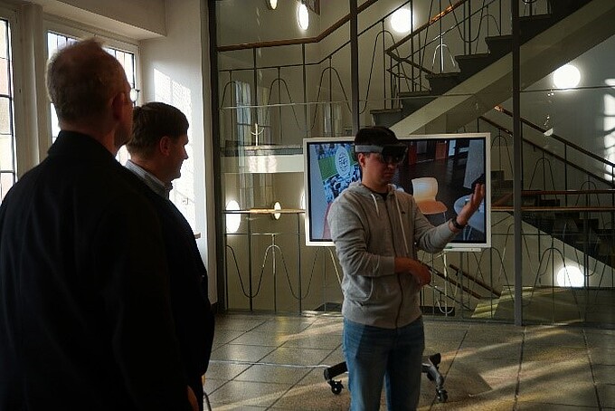 One employee wears AR glasses, other employees watch him.