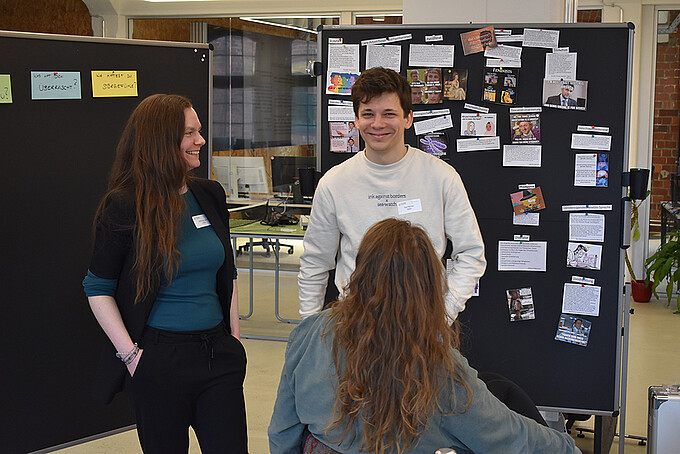 Julia Ochmann and Tom Richter stand in front of pinboards and smile at the participants.