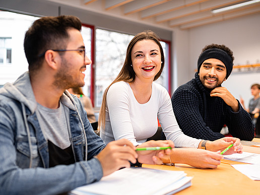 Students with a migration background sit at a desk laughing and chatting.